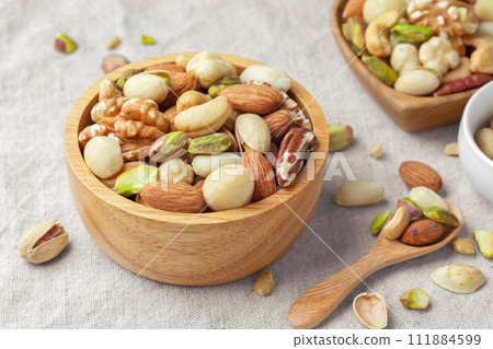 Various nuts in wooden bowl with spoon on linen tablecloth, closeup Various nuts in wooden bowl with spoon on linen tablecloth, closeup 111884599
