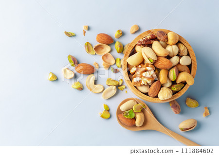 Nuts mixed in wooden bowl with spoon on blue background, top view, copy space 111884602