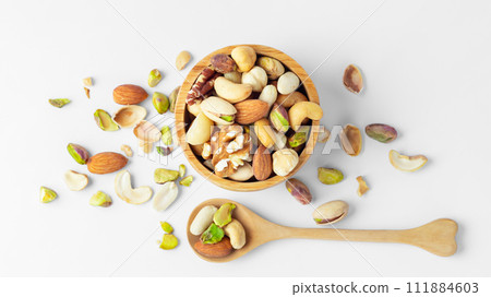 Various nuts in wooden bowl with spoon on white background, top view Various nuts in wooden bowl with spoon on white background, top view 111884603