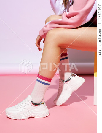 Female legs in stylish sneakers and socks on color background with hard shadow. Female legs in stylish sneakers and socks on color background with hard shadow. 111885147