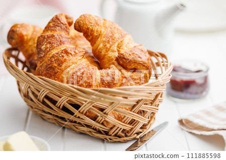 Baked tasty croissants in basket on white table. 111885598
