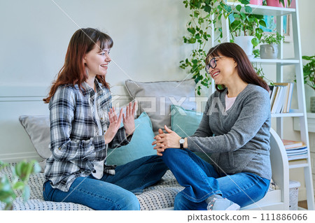Talking mother and teenage daughter sitting together on couch at home 111886066