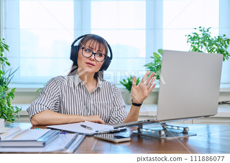 Middle-aged woman in headphones working at computer in home office 111886077