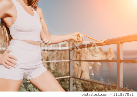 Woman sea fitness. Happy woman with long hair, fitness instructor in white doing stretching and pilates with ribbons in park near the sea. Female fitness yoga routine concept. Healthy lifestyle. Woman sea fitness. Happy woman with long hair, fitness instructor in white doing stretching and pilates with ribbons in park near the sea. Female fitness yoga routine concept. Healthy lifestyle. 111887051