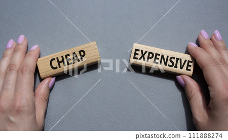 Cheap or Expensive symbol. Concept word Cheap or Expensive on wooden blocks. Businessman hand. Beautiful grey background. Business concept. Copy space 111888274