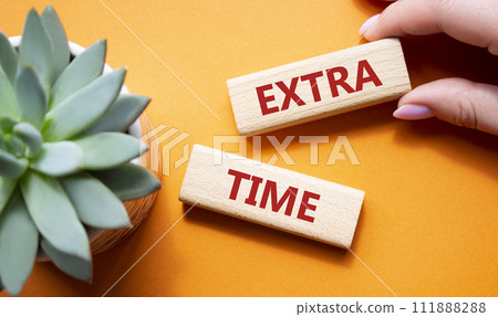 Extra time symbol. Concept word Extra time on wooden blocks. Beautiful orange background with succulent plant. Businessman hand. Business and Extra time concept. Copy space Extra time symbol. Concept word Extra time on wooden blocks. Beautiful orange background with succulent plant. Businessman hand. Business and Extra time concept. Copy space 111888288