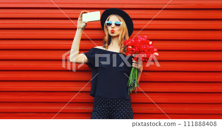 Beautiful young woman taking selfie with smartphone holding bouquet of red rose flowers 111888408