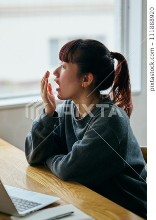 一位年輕女子在辦公桌前打哈欠,看起來很睏 一位年輕女子在辦公桌前打哈欠,看起來很睏 111888920