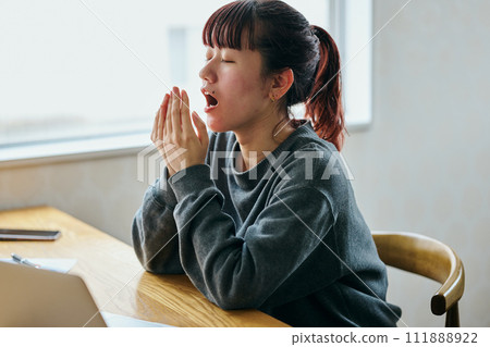 A young woman yawning at her desk and looking sleepy 111888922