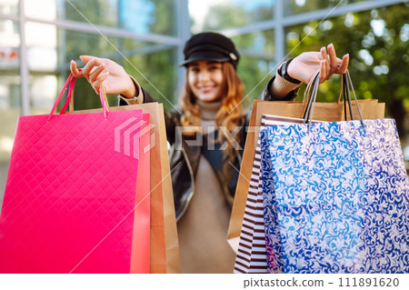 Smiling woman with shopping bags using her phone. Young woman after shopping on the city street. 111891620