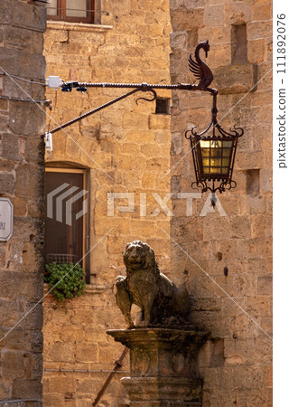 A lion statue and an old vintage street light in the city of Volterra A lion statue and an old vintage street light in the city of Volterra 111892076
