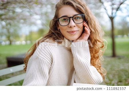 Attractive woman enjoys scent of flowers in spring garden. Concept of relaxation, spring, youth. 111892337
