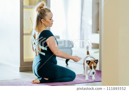 Beautiful mature mid adult body positive lady in sportwear leading healthy lifestyle doing yoga whilst caring for furry friend. Beautiful mature mid adult body positive lady in sportwear leading healthy lifestyle doing yoga whilst caring for furry friend. 111893552