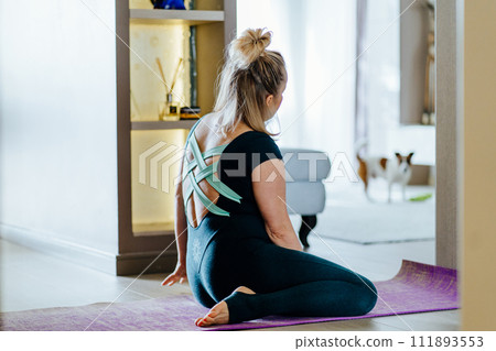 Fit sporty healthy mature middle age body positive woman call the dog while sit on mat. Fit and healthy, home fitness concept. Fit sporty healthy mature middle age body positive woman call the dog while sit on mat. Fit and healthy, home fitness concept. 111893553