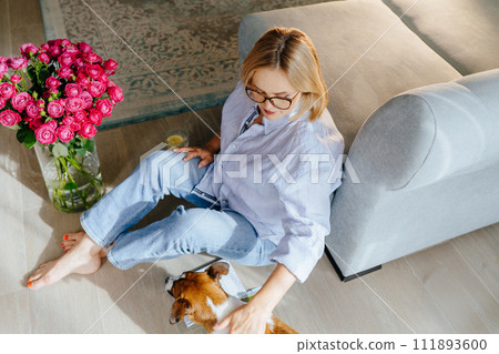 A bouquet of roses in a glass vase nearby. adult beautiful female people - enjoying quiet lifestyle indoor caressing playing with her adorable jack Russell terrier. A bouquet of roses in a glass vase nearby. adult beautiful female people - enjoying quiet lifestyle indoor caressing playing with her adorable jack Russell terrier. 111893600
