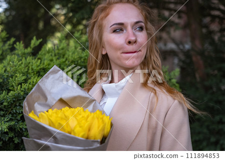 Girl holding bouquet of tulips and looking into the distance. Woman with yellow flowers outside waiting for someone licking her lips. Girl holding bouquet of tulips and looking into the distance. Woman with yellow flowers outside waiting for someone licking her lips. 111894853