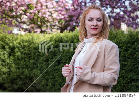 Serious young woman in white blouse looking to the camera. Woman of European appearance. Successful business woman in spring park. Serious young woman in white blouse looking to the camera. Woman of European appearance. Successful business woman in spring park. 111894854