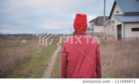 A sad teenage girl in red clothes is walking down the street. View from the back. 111896671