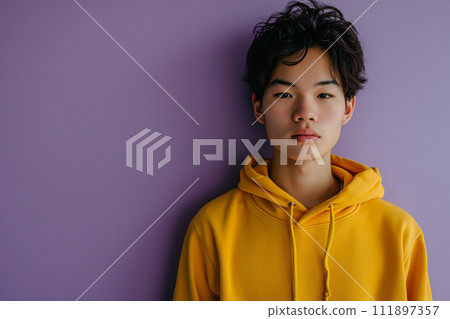 Asian serious teenage boy wearing yellow hoodie on purple background 111897357