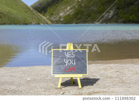 Motivational and Yes you can symbol. Concept words Yes you can on beautiful black chalk blackboard. Beautiful mountain lake background. Business motivational and Yes you can concept. Copy space. 111898302