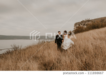 couple wedding newlyweds in walk hug kissing on tall grass on mountain above the river 111898667