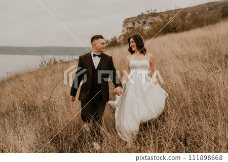 couple wedding newlyweds in walk hug kissing on tall grass on mountain above the river couple wedding newlyweds in walk hug kissing on tall grass on mountain above the river 111898668