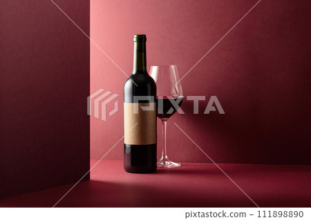 Bottle and glass of red wine on a red background. 111898890