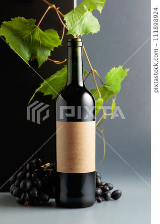 Bottle of red wine with blue grapes and vine branches. 111898924