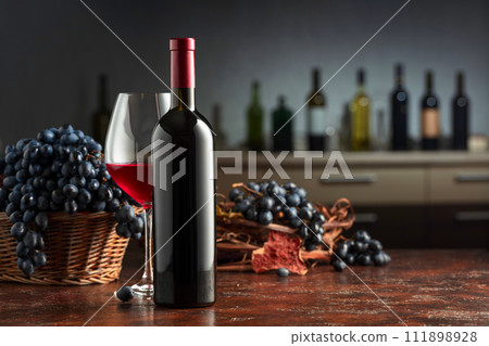 Bottle and glass of red wine with grapes on a vintage table. Bottle and glass of red wine with grapes on a vintage table. 111898928