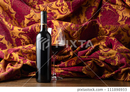 Bottle and glass of red wine and retro tapestry with floral ornament. Bottle and glass of red wine and retro tapestry with floral ornament. 111898933