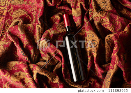 Bottle of red wine on a retro tapestry with dark red and golden floral ornament. Bottle of red wine on a retro tapestry with dark red and golden floral ornament. 111898935