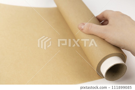 Unrolling a roll of parchment paper. A woman's hand is unrolling baking paper. The concept of baking. 111899085
