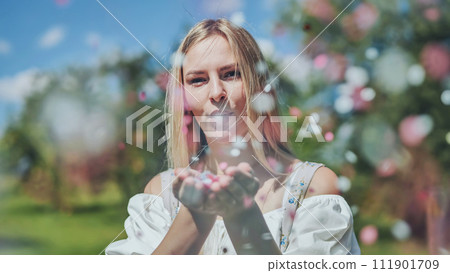 A girl blows a multi-coloured paper confetti out of her hands. 111901709