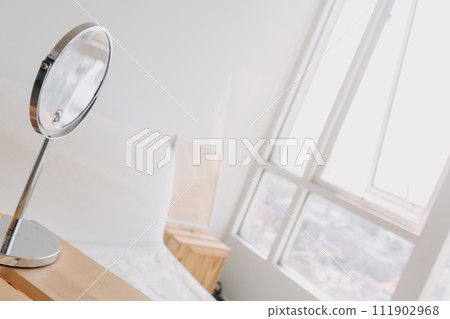 A mirror is sitting on a table next to a window in a bedroom 111902968