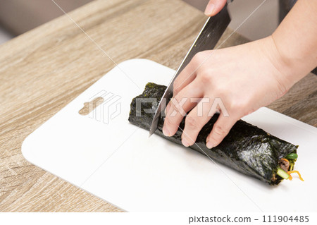 Woman's hands cutting sushi rolls Woman's hands cutting sushi rolls 111904485