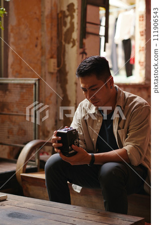 Frowning man looking at his broken analog camera, thinking how to fix it Frowning man looking at his broken analog camera, thinking how to fix it 111906543