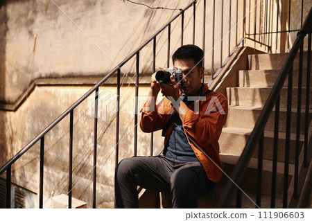 Photographer sitting on steps and taking photos in old decaying building 111906603