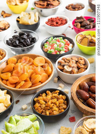 Mix of healthy dried sweet fruits and berries in various bowl plates on light kitchen background. Mix of healthy dried sweet fruits and berries in various bowl plates on light kitchen background. 111907348