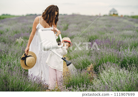 Mother with little daughter on lavender background. Beautiful woman and cute baby playing in meadow field. Family holiday in summer day. 111907699