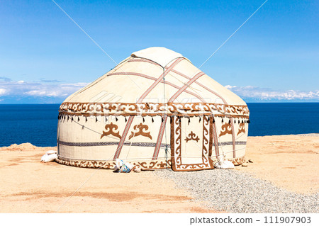 Traditional Yurt. National nomadic old house of Central Asia with blue sky on background. Issyk Kul high alpine lake in the Tian Shan Mountains. Kyrgyz ger camp for tourists of Kyrgyzstan. Traditional Yurt. National nomadic old house of Central Asia with blue sky on background. Issyk Kul high alpine lake in the Tian Shan Mountains. Kyrgyz ger camp for tourists of Kyrgyzstan. 111907903