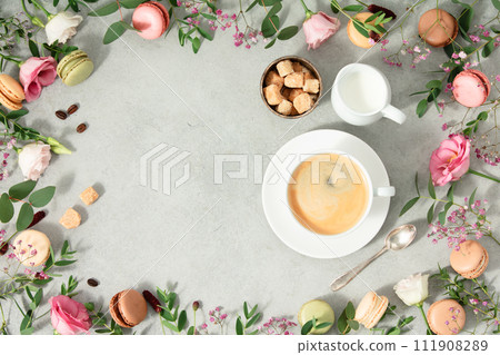 White cup of coffee and Frame made of Spring flowers and different types of macaroons White cup of coffee and Frame made of Spring flowers and different types of macaroons 111908289