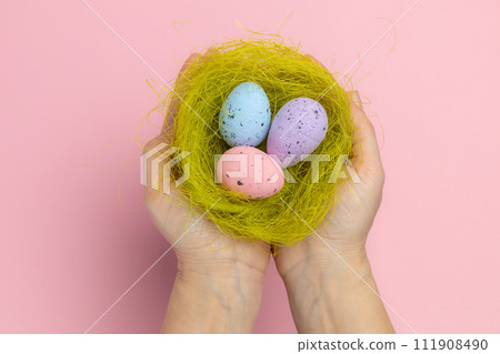 Female hands holding a nest with the Easter eggs. 111908490