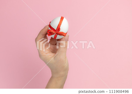 Easter egg with a red ribbon in a female hand. Easter egg with a red ribbon in a female hand. 111908496