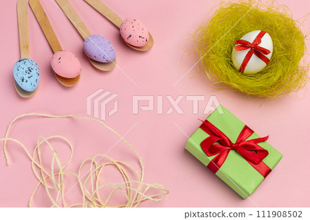 Colored Easter eggs on wooden spoons with a nest and a gift box. Colored Easter eggs on wooden spoons with a nest and a gift box. 111908502