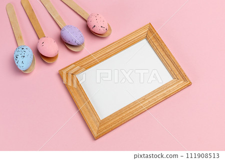 Colored Easter eggs on wooden spoons with a photo frame. 111908513