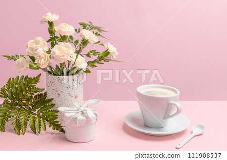 Bouquet of carnations in a vase with a gift box and a cup of coffee. Bouquet of carnations in a vase with a gift box and a cup of coffee. 111908537