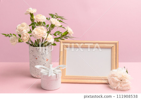 Bouquet of carnations in a vase with a gift box and a photo frame. 111908538
