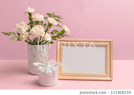 Bouquet of carnations in a vase with a gift box and a photo frame. Bouquet of carnations in a vase with a gift box and a photo frame. 111908539