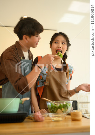 Smiling man feeding wife with vegetable salad, happy couple spending weekend time together at home Smiling man feeding wife with vegetable salad, happy couple spending weekend time together at home 111909814