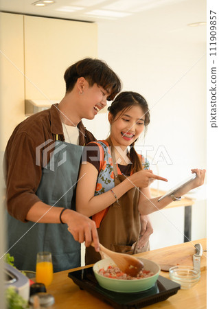 Portrait of happy young couple wearing aprons cooking together in the kitchen at home Portrait of happy young couple wearing aprons cooking together in the kitchen at home 111909857